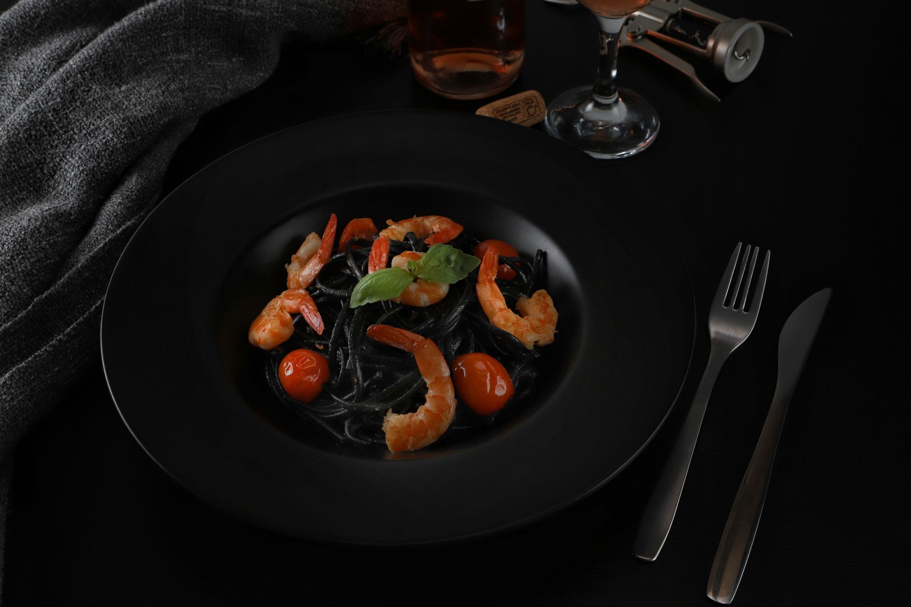 Spaghetti al nero di seppia con gamberi e pomodorini su un piatto nero.