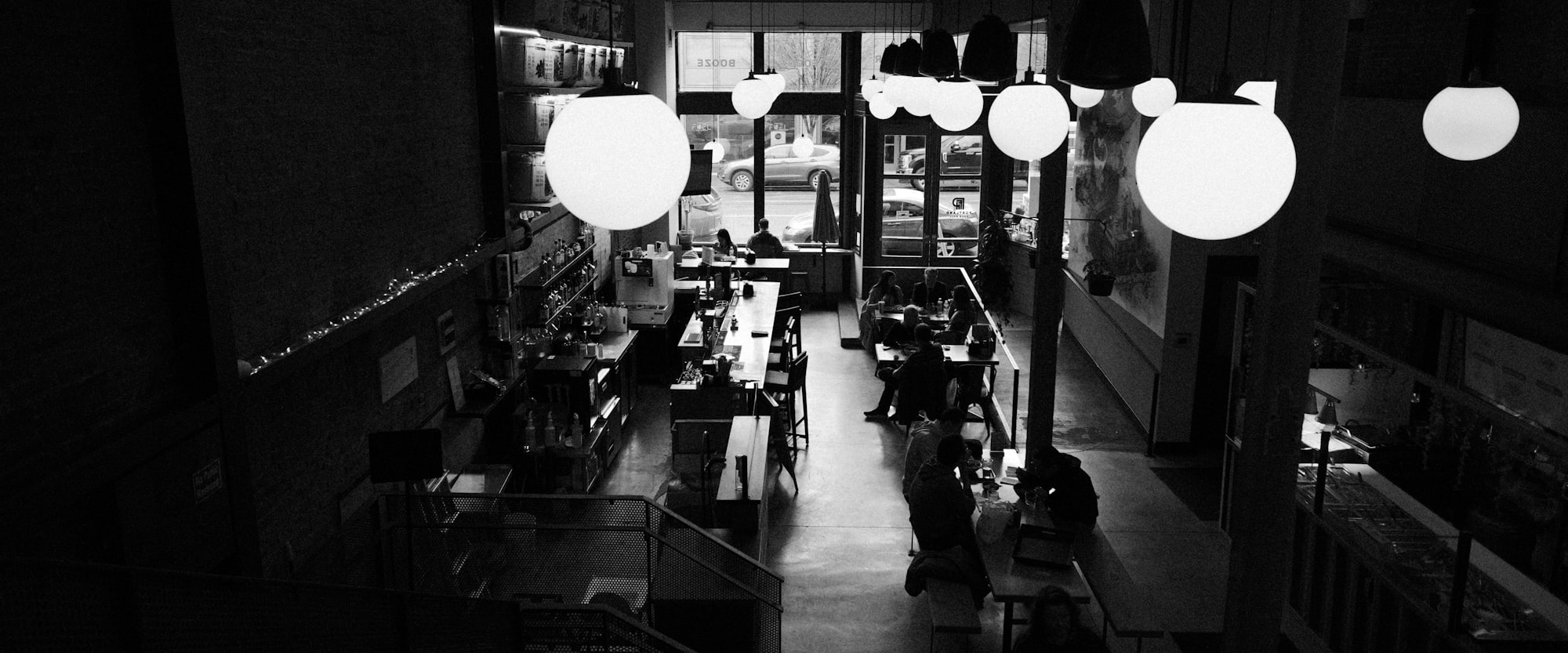 Sala da pranzo in bianco e nero, lampade a globo accese contro il fondo scuro.